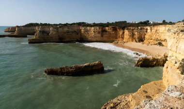 Kızıl kayalıkları ve kayalıkları olan güzel kumlu bir sahil. Günbatımında Praia do Barranco, Praia do Pontal, Algarve, Portekiz 'deki Atlantik kıyısında sığ dalgalarla birlikte. Yüksek kalite fotoğraf