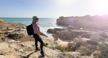 Güneşli ve rüzgarlı bir yaz gününde Atlantik Okyanusu 'nun üzerinde uçurumun kenarında duran orta yaşlı güzel bir yürüyüşçü kadın. Arkadan bak. Yüksek kalite fotoğraf