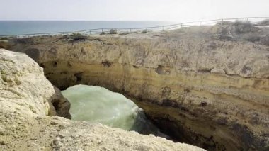 Okyanusun manzaralı bir manzarası kayalık bir mağaranın açılması, dalgaların parlak mavi bir gökyüzünün altında, tüylü bulutların altında bir uçuruma çarpması. Yüksek kalite fotoğraf