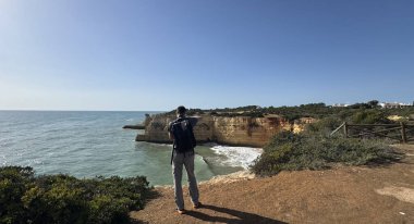 Gezgin, seyahat fotoğraflı sırt çantasıyla uçurumların harika fotoğraflarını çekiyor. Gezgin fotoğrafçı, fotoğraf makinesinin görüş açısıyla deniz manzarası çekiyor. panoramik seyahat fotoğrafçılığı. Yüksek kalite fotoğraf