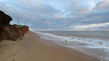 Atlantik 'te kumlu bir sahil. Kum taşı kayalıkları olan bir sahilin gün batımında manzara. Albufeira, Algarve, Portekiz yakınlarındaki Praia 'nın sarı sahilinde gelgit var. Yüksek kalite fotoğraf