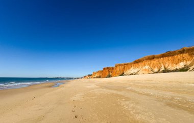 Atlantik 'teki kumlu sahil. Kum taşı kayalıkları olan bir sahilin gün batımında manzara. Albufeira, Algarve, Portekiz yakınlarındaki Praia 'nın sarı sahilinde gelgit var. Yüksek kalite fotoğraf