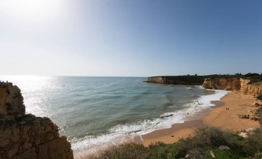 Kumlu Algarve plajı, dramatik bir gökyüzü altında kaya oluşumlarına çarpan dalgalar. Huzurlu bir manzara, doğayı keşfetmek, kıyı titreşimleri. Yüksek kalite fotoğraf