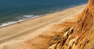 Atlantik 'teki kumlu sahil. Kum taşı kayalıkları olan bir sahilin gün batımında manzara. Albufeira, Algarve, Portekiz yakınlarındaki Praia 'nın sarı sahilinde gelgit var. Yüksek kalite fotoğraf