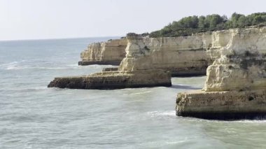 Dalgalar Praia da Morena, Algarve, Portekiz yakınlarındaki kayalık kıyı şeridine çarpıyor, açık mavi gökyüzü altında deniz manzarası var. Yüksek kalite fotoğraf
