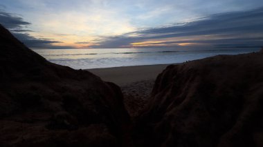 Kızıl kayalıkları ve kayalıkları olan güzel kumlu bir sahil. Günbatımında Praia de Loule Velho, Algarve, Portekiz 'de Atlantik kıyısında sığ dalgalarla birlikte. Yüksek kalite fotoğraf