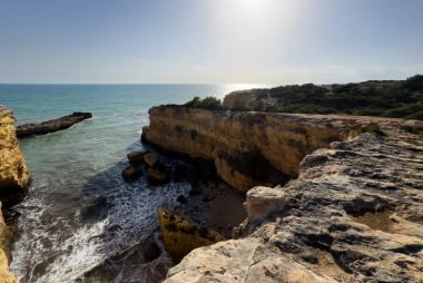 Okyanusun manzaralı bir manzarası kayalık bir mağaranın açılması, dalgaların parlak mavi bir gökyüzünün altında, tüylü bulutların altında bir uçuruma çarpması. Yüksek kalite fotoğraf