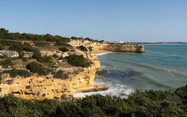 Kızıl kayalıkları ve kayalıkları olan güzel kumlu bir sahil. Günbatımında Praia do Barranco, Praia do Pontal, Algarve, Portekiz 'deki Atlantik kıyısında sığ dalgalarla birlikte. Yüksek kalite fotoğraf