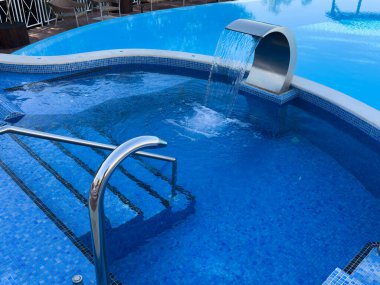 Boş yüzme havuzu, şelale jeti, jakuzi, kaplıca ve sağlık merkezi. Sahil tatili, otel konsepti. Mavi temiz deniz suyu havuzunda yansıma. Şelaleli kaplıcada rahatlama havuzu. Yüksek kalite fotoğraf