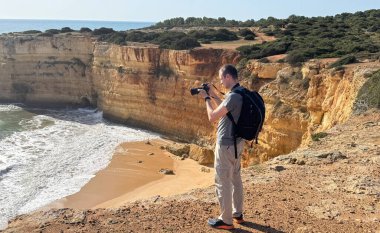 Gezgin, seyahat fotoğraflı sırt çantasıyla uçurumların harika fotoğraflarını çekiyor. Gezgin fotoğrafçı, fotoğraf makinesinin görüş açısıyla deniz manzarası çekiyor. panoramik seyahat fotoğrafçılığı. Yüksek kalite fotoğraf
