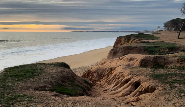 Kızıl kayalıkları ve kayalıkları olan güzel kumlu bir sahil. Günbatımında Praia de Loule Velho, Algarve, Portekiz 'de Atlantik kıyısında sığ dalgalarla birlikte. Yüksek kalite fotoğraf