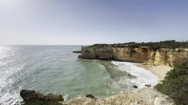 Dalgalar Praia da Morena, Algarve, Portekiz yakınlarındaki kayalık kıyı şeridine çarpıyor, açık mavi gökyüzü altında deniz manzarası var. Yüksek kalite fotoğraf