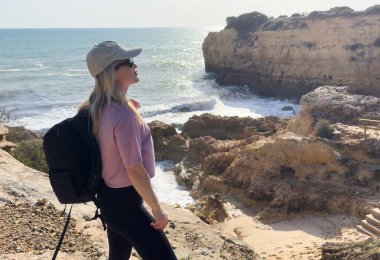 Kayalıkların yanındaki sahilde yürüyüş yapan bir kadın. Arkadan bak. Praia de Albandeira, Portekiz 'in Algarve sahilinde bir plaj. Yüksek kalite fotoğraf