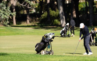 Erkek golfçü, güneşli bir günde kum havuzundan golf arabası ve diğer oyuncularla topa vuruyor. Yüksek kalite fotoğraf