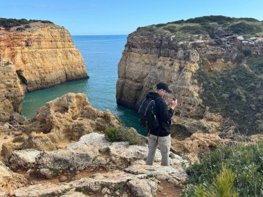 Bir uçurumun tepesine tırmanan genç bir adam, Portekiz, Avrupa 'da geniş bir açık okyanusun manzarasının tadını çıkarıyor. Yüksek kalite fotoğraf