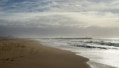 Hafif okyanus dalgalarının kıyıya vurduğu kumlu bir sahil altın öğleden sonra güneş ışığı altında soluk uzak tepeler hafif bulutlu bir gökyüzünün altında ufuk çizgisi oluştururken. - Evet. Yüksek kalite fotoğraf