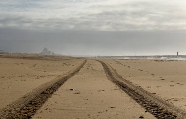 Kum formundaki taze lastik izleri uzaklığa doğru giden paralel çizgilere çarpıyor. Işık güçlü gölgeler ve dokular yaratır. Yüksek kalite fotoğraf