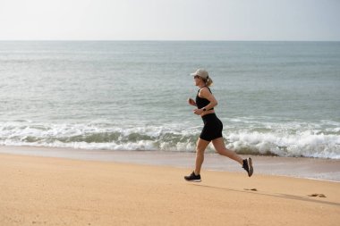 Genç bir kadın sabah deniz kıyısında koşuyor. Plaj boyunca koşan sağlıklı bir kadın. Yüksek kalite fotoğraf