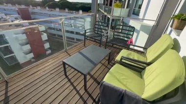 Rahat koltukları, dekoratif bitkileri, küçük bir masası ve bulutlu bir günde modern konut binalarına bakan manzarası olan davetkar bir balkon alanı. Yüksek kalite fotoğraf