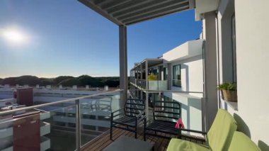 Rahat koltukları, dekoratif bitkileri, küçük bir masası ve bulutlu bir günde modern konut binalarına bakan manzarası olan davetkar bir balkon alanı. Yüksek kalite fotoğraf