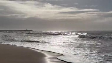 Hafif okyanus dalgalarının kıyıya vurduğu kumlu bir sahil altın öğleden sonra güneş ışığı altında soluk uzak tepeler hafif bulutlu bir gökyüzünün altında ufuk çizgisi oluştururken. - Evet. Yüksek kalite fotoğraf