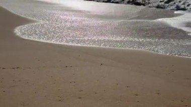 Yakın çekim dalgası, altın gün batımında kumsaldaki bir kumsala çarpıyor. Dalgalı deniz. Ses ile normal hız. Yüksek kalite 4k görüntü