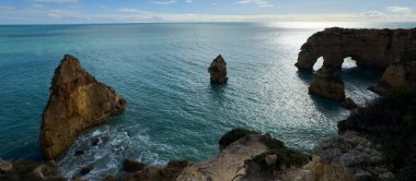 Altın kayalar, parçalı bulutlu gökyüzünün altında sakin mavi denizle buluşur ve Portekiz 'in güzel sahil şeridini gözler önüne serer. Yüksek kalite fotoğraf