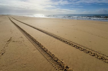 Kum formundaki taze lastik izleri uzaklığa doğru giden paralel çizgilere çarpıyor. Işık güçlü gölgeler ve dokular yaratır. Yüksek kalite fotoğraf