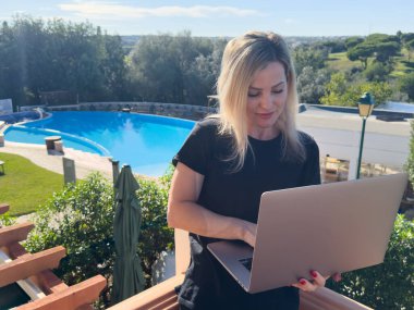 Kadın dizüstü bilgisayarda uzaktan çalışıyor, klavye yazarken yüzme havuzunda güneşleniyor. Yüksek kalite fotoğraf