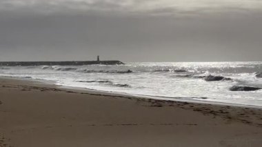 Hafif okyanus dalgalarının kıyıya vurduğu kumlu bir sahil altın öğleden sonra güneş ışığı altında soluk uzak tepeler hafif bulutlu bir gökyüzünün altında ufuk çizgisi oluştururken. - Evet. Yüksek kalite fotoğraf