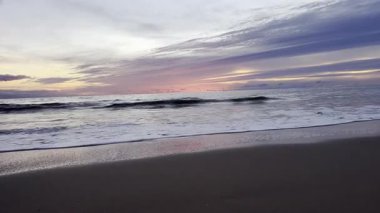 Gökyüzünde harmanlanan parlak altın ve mor tonlarıyla okyanusun üzerinde gün batımı ve renkleri yansıtan sakin dalgalar kıyı manzarasının huzurlu ve resimsel bir görüntüsünü sunuyor. Tayland. - Evet. Yüksek kalite 4k görüntü