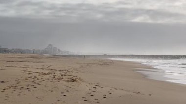Hafif okyanus dalgalarının kıyıya vurduğu kumlu bir sahil altın öğleden sonra güneş ışığı altında soluk uzak tepeler hafif bulutlu bir gökyüzünün altında ufuk çizgisi oluştururken. - Evet. Yüksek kalite fotoğraf