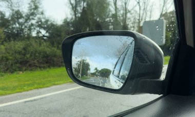 Yağmurlu bir gün, ıslak yolda bulanık beyaz bir araçla araba yan aynası. Ulaşım, sürüş güvenliği, seyahat ve otomotiv editörlüğü veya ticari içerik için mükemmel. Yüksek kalite fotoğraf