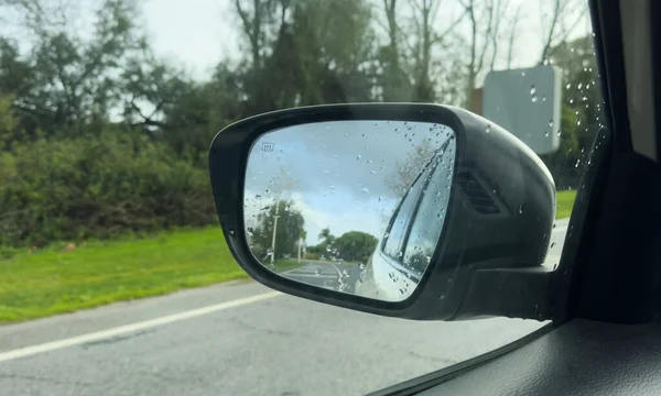 Yağmurlu bir gün, ıslak yolda bulanık beyaz bir araçla araba yan aynası. Ulaşım, sürüş güvenliği, seyahat ve otomotiv editörlüğü veya ticari içerik için mükemmel. Yüksek kalite fotoğraf