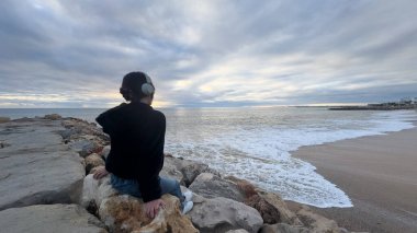 Kapüşonlu ve bereli biri Portekiz sahilinde sakin bir gün batımını seyrediyor. Yüksek kalite fotoğraf