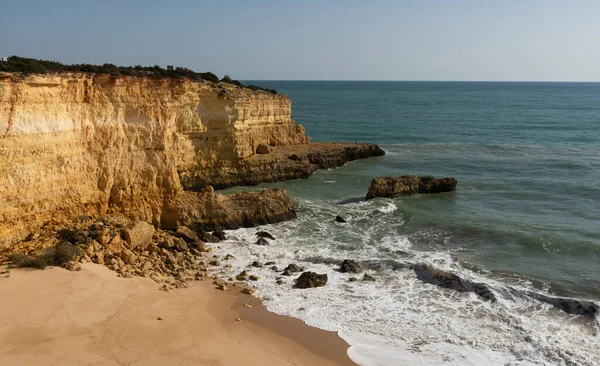 Kızıl kayalıkları ve kayalıkları olan güzel kumlu bir sahil. Günbatımında Praia do Barranco, Praia do Pontal, Algarve, Portekiz 'deki Atlantik kıyısında sığ dalgalarla birlikte. Yüksek kalite fotoğraf
