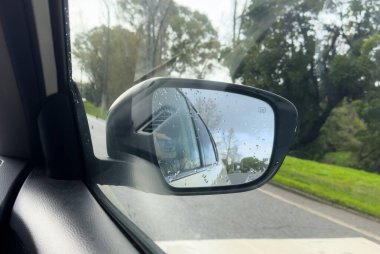 Yağmurlu bir gün, ıslak yolda bulanık beyaz bir araçla araba yan aynası. Ulaşım, sürüş güvenliği, seyahat ve otomotiv editörlüğü veya ticari içerik için mükemmel. Yüksek kalite fotoğraf