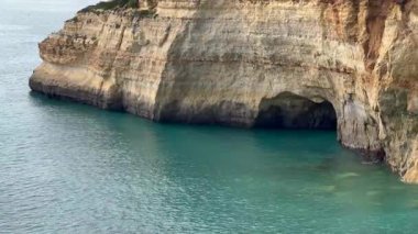 Deniz manzarası ve bir kıyı mağarasının girişiyle çerçevelenmiş kayalık kıyı şeridi. Doğal bileşim, okyanus suyu, engebeli uçurumlar ve berrak mavi gökyüzünü birleştirerek keşfin ve manzaranın güzelliğini sembolize eder. Yüksek kalite fotoğraf