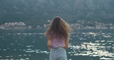 Mutlu esmer kadın iskelede koşar, ellerini kaldırır ve doğa manzarasının tadını çıkarır. Arkadan bak. Koyun ve dağların manzarası.