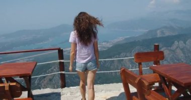 Kıvırcık saçlı mutlu turist uçuruma doğru yürüyor. Durur ve doğayı düşünür. Arkadan bak. Yükseklerden dağlara ve koylara bak..