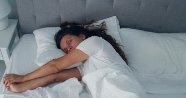 Günaydın Uyan. Çekici, gülümseyen genç bir kadın uyandığında tamamen beyaz bir yatakta dinleniyor. Güzel, sağlıklı bir manken kız. Kollarını esnetiyor. Yatakta uzanıyor ve evde dinleniyor..