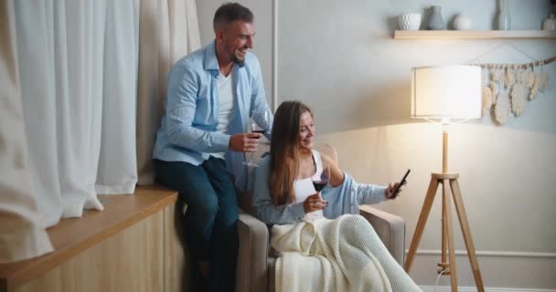 Ein Ehepaar feiert den Urlaub zu Hause, trinkt Wein, macht ein Selfie und hat Spaß beim Plaudern. Frauen- und Männerporträt — Stockvideo