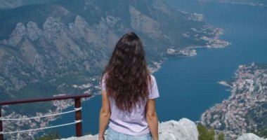 Kıvırcık saçlı mutlu bir turist uçurumun kenarında masraflı oluyor. Ellerinizi kaldırın ve doğayı düşünün. Arkadan bak. Yükseklerden dağlara ve koylara bak..