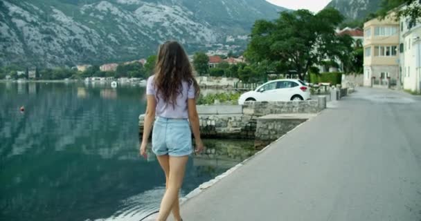Šťastná brunetka žena procházky po městě v blízkosti mola, a má výhled na přírodu. Pohled na záliv a hory. — Stock video