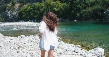 Genç narin kadın turist bir dağ gölüne koşar ve ellerini kaldırır. Dağ ve göl manzarası. Arka plan