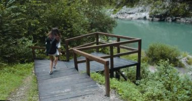 Sırt çantalı mutlu bir turist dağ gölüne doğru koşuyor. Kadın ellerini kaldırır ve manzaranın tadını çıkarır..