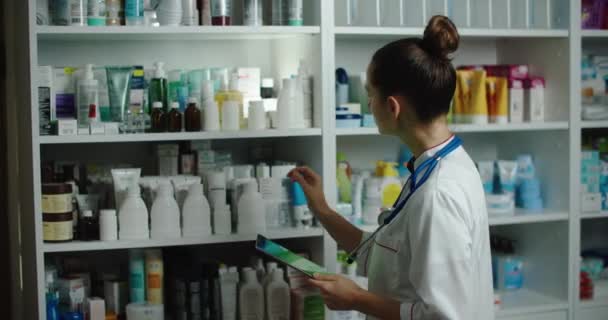 Comprobación de medicamentos de reclutamiento en una farmacia, comprobando con una tableta. Mujer farmacia comprueba los medicamentos, mira una tableta con una pantalla verde. — Vídeo de stock