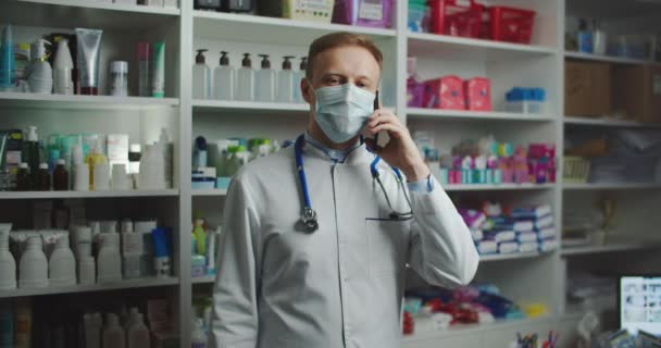 A pharmacist with a medical mask at a pharmacy advises a client by phone. Telephone call. — Video Stock
