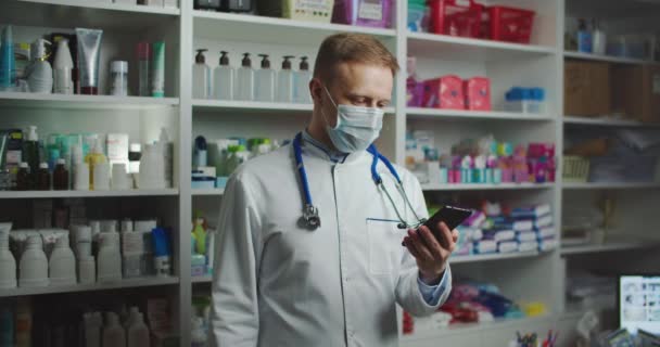 A pharmacist with a medical mask at a pharmacy advises a client by phone. Telephone call. — Video