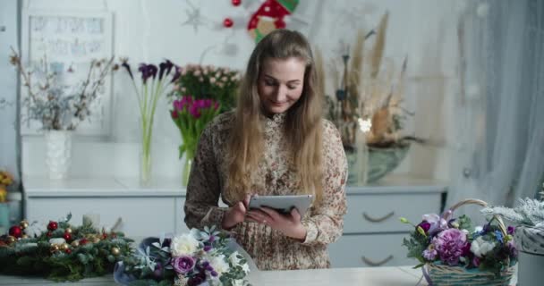 Close up portrait of Caucasian happy woman florist browsing on tablet at floral store and smiling. Beautiful female entrepreneur of flower shop tapping on device at work. Floristry concept — Stock Video